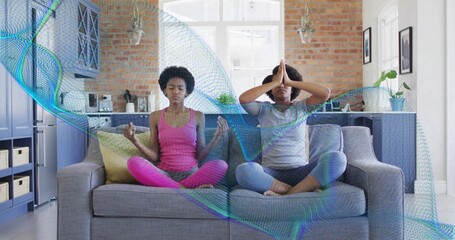 Fototapeta premium Meditating mother-daughter sitting on grey sofa in home kitchen in pink and grey with teal overlay