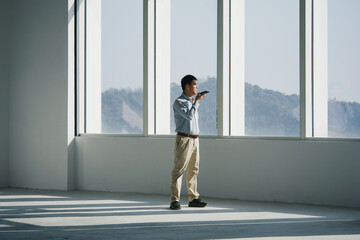 Man standing by large window talking on phone while gazing at distant mountains
