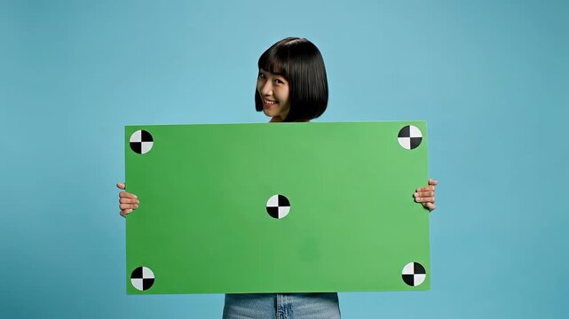 Young woman holding green chroma key board with tracking markers