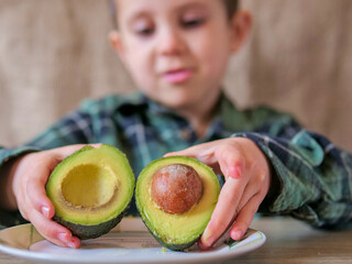 Child Hands Holding Two Halves of Ripe Avocado with and without Pit on Plate — Fresh Avocado Cross Section, Healthy Food Concept with Kid in Background © light
