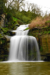 Obraz premium Silky waterfall in lush forest with mossy rocks and flowing stream, long exposure nature landscape