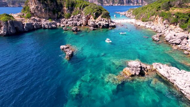 Corfu Limni beach 4k drone fly backward from turquoise water to deep blue sea. Scenic aerial view of rocky coast and crystal clear ocean in Greece. Rent boats Greece coastal scenery