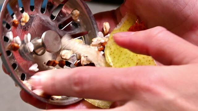 A close-up of someone cleaning a kitchen sink drain strainer filled with food waste.