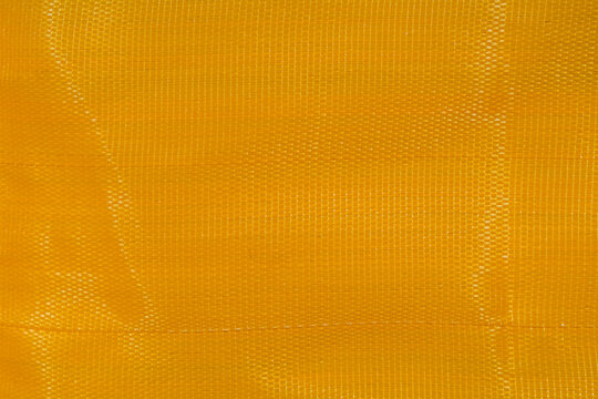 Close-up of yellow woven polypropylene mesh texture background. Industrial plastic fabric pattern with durable grid structure for packaging, construction, and design concepts