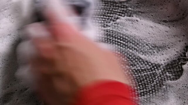 Hand scrubbing a black frying pan with soap, creating circular patterns in foam while cleaning, showcasing the progression of the cleaning process in a kitchen setting