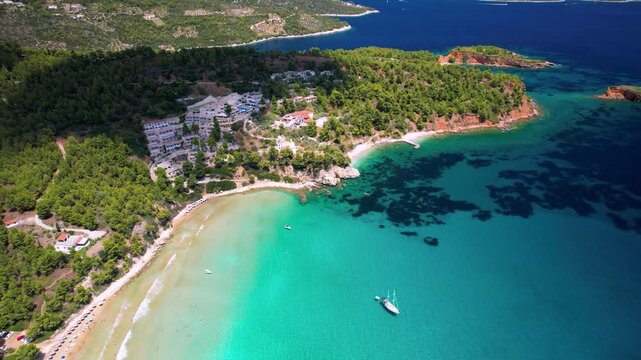 Chrisi Milia Alonissos 4k drone top down view of golden sand beach and turquoise sea in Greece. Aerial view of luxury white hotel on hill and yacht in bay. Tropical paradise scenery in Sporades