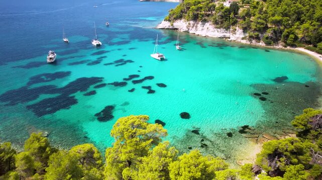 Alonissos Milia beach 4k drone of turquoise bay and luxury yachts in Greece. Aerial panorama of emerald water and pine trees forest. Sporades islands cinematic travel scenery
