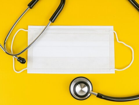 Stethoscope and medical mask on yellow background, healthcare and safety concept