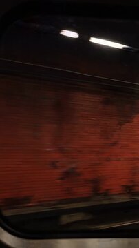 Cinematic motion blur of a vibrant red subway tunnel wall seen through a moving train window with overhead fluorescent lighting in a vertical orientation.