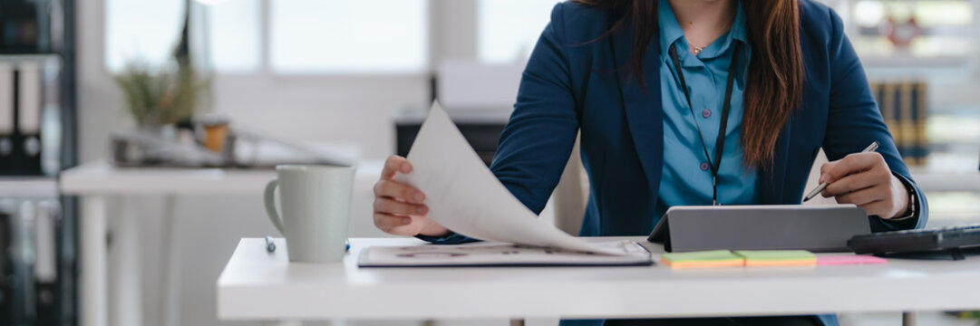 Confident businesswoman sitting at modern office desk reviewing reports and focusing on company tasks
