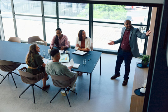 Mature businessman in smart casual presenting to diverse team sitting at conference table in office