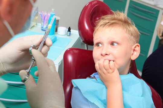 Childish fear. A cute little boy sits in the dentist's chair and covers his mouth with his hand in fear, fearing the syringe in his doctor's hands.