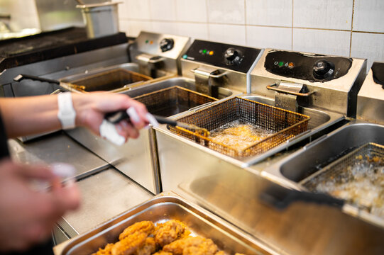 Professional chef deep frying golden crispy chicken wings in a commercial kitchen deep fryer, busy restaurant food preparation.