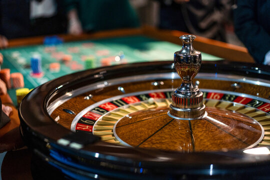 Close view of roulette wheel spinning in casino with players and betting table in background. Gambling, risk and luck concept.