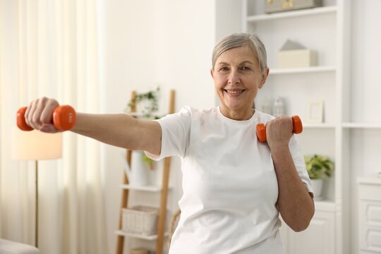 Senior woman exercising with dumbbells at home. Fitness and sport
