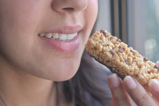 Una joven atleta  comiendo una barra de prote&iacute;nas como refrigerio.