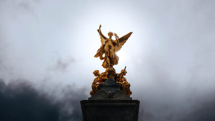 Plakat Golden winged statue against dramatic stormy grey sky low angle view