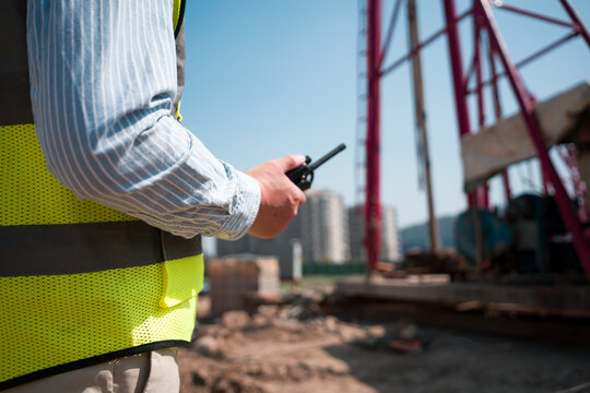 Construction worker holding walkie-talkie while directing on-site operations at a building site