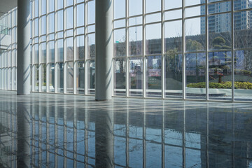 Naklejka premium Modern architectural interior with glass curtain wall and reflective polished floor capturing urban landscape