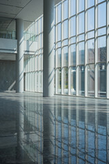 Naklejka premium Modern architectural interior with glass curtain wall and dramatic light shadows on reflective floor