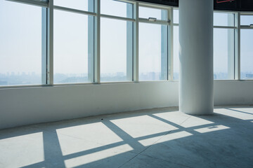 Naklejka premium Empty modern office space with floor-to-ceiling windows casting geometric shadows on concrete floor and white column