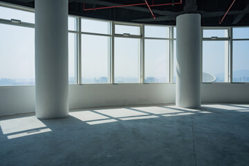 Obraz premium Spacious empty office interior with floor-to-ceiling windows, white columns, and natural light casting geometric shadows