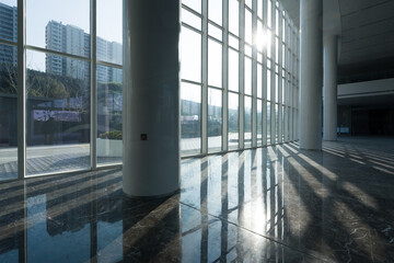 Obraz premium Sunlight streams through glass curtain wall in modern building lobby with reflective marble floor and structural columns