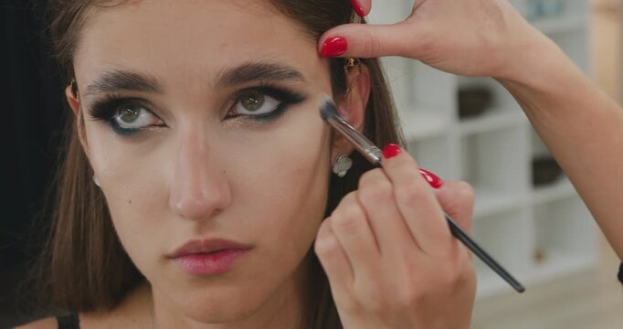 Close-up shot of a makeup artist applying concealer under the client eyes with a brush. Dramatic makeup.