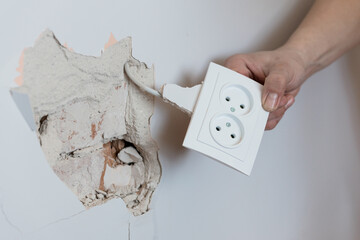 Electrician Removing Broken White Wall Socket Exposing Cracked Plaster and Electrical Wiring in...