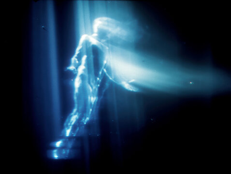 A glowing, light-based humanoid figure flying through a dark astral realm, portrayed in a low-resolution, vintage 35mm film style with VHS artifacts, long exposure distortions, and heav - AI-Generated