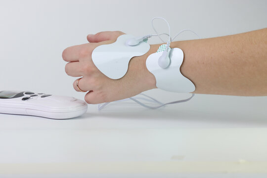 A person's wrist and hand are shown with TENS unit electrode pads attached for pain relief therapy