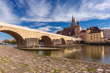 Obraz premium Historic stone bridge over the Danube River in Regensburg, Bavaria, under a bright summer sky.