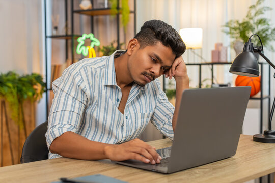 Indian man at home shuts laptop with fast hand says enough and breathes out and wants time without tech. Arabian guy at desk looks aside rubs neck and plans short pause for focus recovery and mind zen