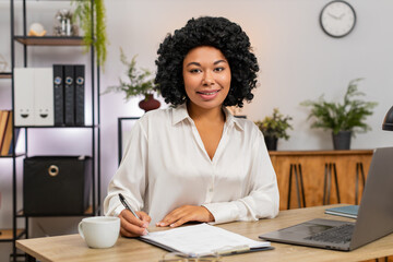African American businesswoman at home office signs major documents nodding satisfied securing big...