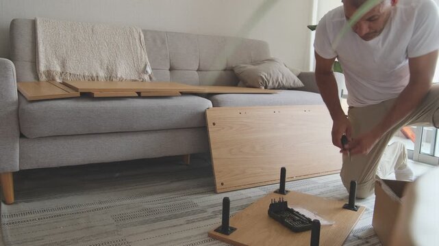 Diligent man using a screwdriver to assemble a piece of wooden furniture in his living room