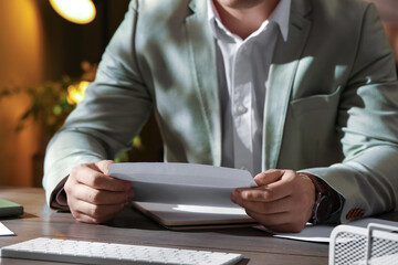 Man opening envelope with letter at wooden table indoors, closeup