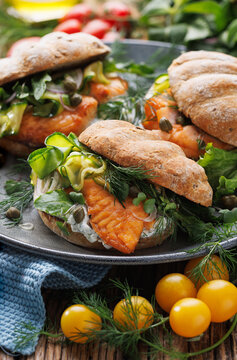 Salmon sandwich with veggies and yogurt sauce on a ceramic plate, close up view