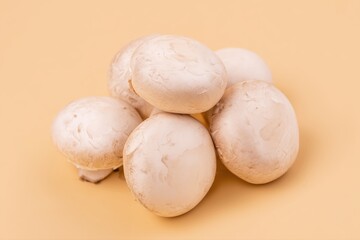 Fototapeta premium Fresh whole white button mushrooms grouped on a warm beige background, soft lighting, minimal shadow, clean composition.