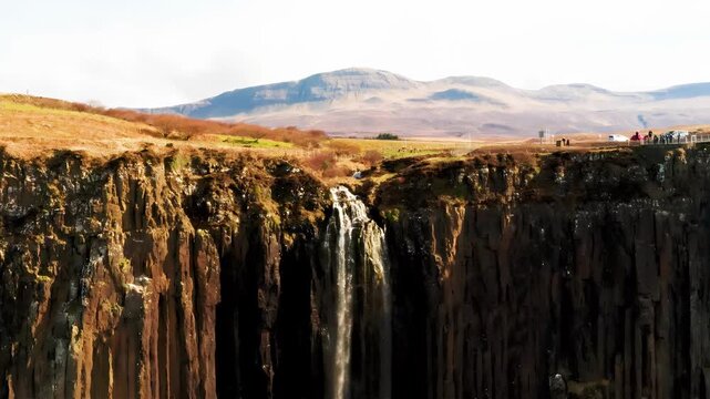 Dramatic waterfall cascades down basalt columns with tourists observing from above
