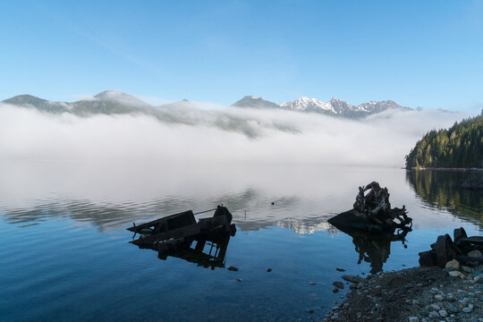 Canada, BC, Vancouver Island, Telegraph Cove.  Fog lays over the face of Nimpkish Lake.  Old logging equipment left abandoned in the lake 