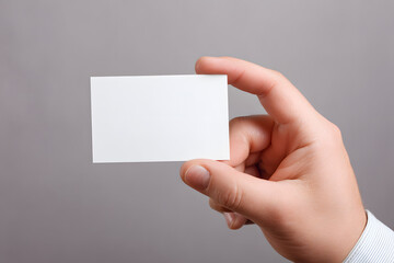 Fototapeta premium Person holds blank card with one hand against plain background in indoor setting