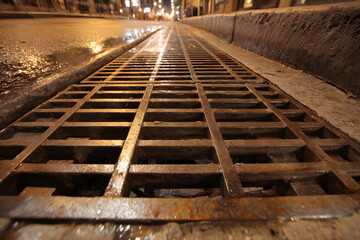 Fototapeta premium Metal grating on a city street next to wet pavement in the evening light