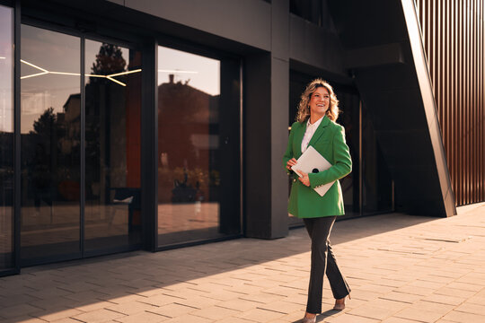 Businesswoman walking confident outside modern office building with laptop