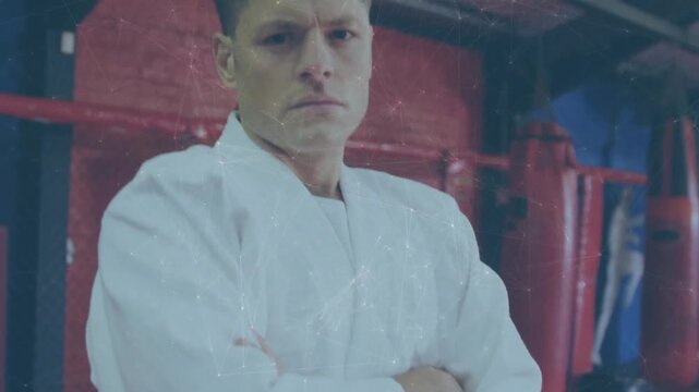 Camera pulling back, coach in gi standing arms crossed revealing black belt and bags, showing focus