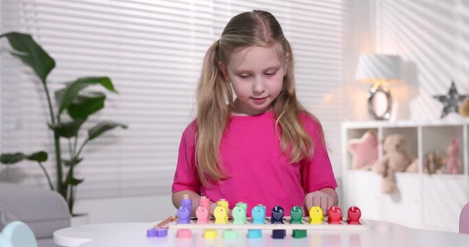 Little girl playing with educational toy at table indoors