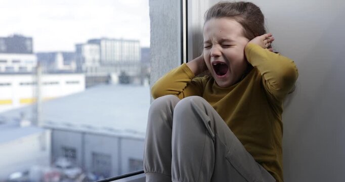 Autism. Little girl screaming on window sill indoors