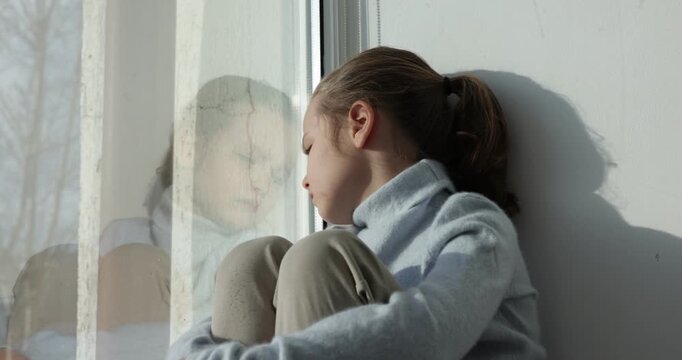 Autism. Little girl on window sill indoors