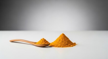 Yellow turmeric powder, spoon, and pile on a white surface with a grey gradient background