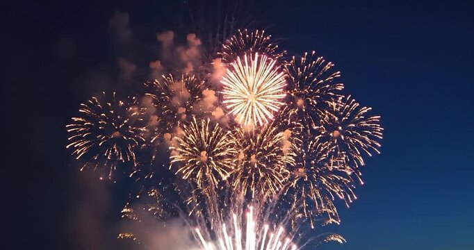 Multiple golden fireworks explode brightly in dark night sky