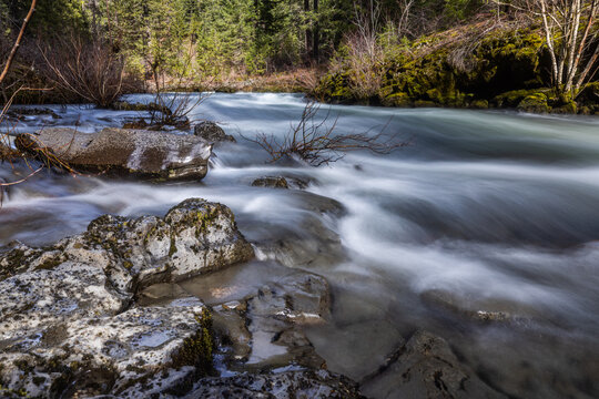 Rogue River above Union Creek, Oregon rushes over jagged stones. Mossy banks glow in golden sunlight. Nature's force moves through rocky terrain.